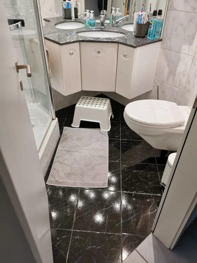 Kleines Bad mit Eckwaschtisch, Wand-WC und schwarzem Marmorboden vor dem Umbau