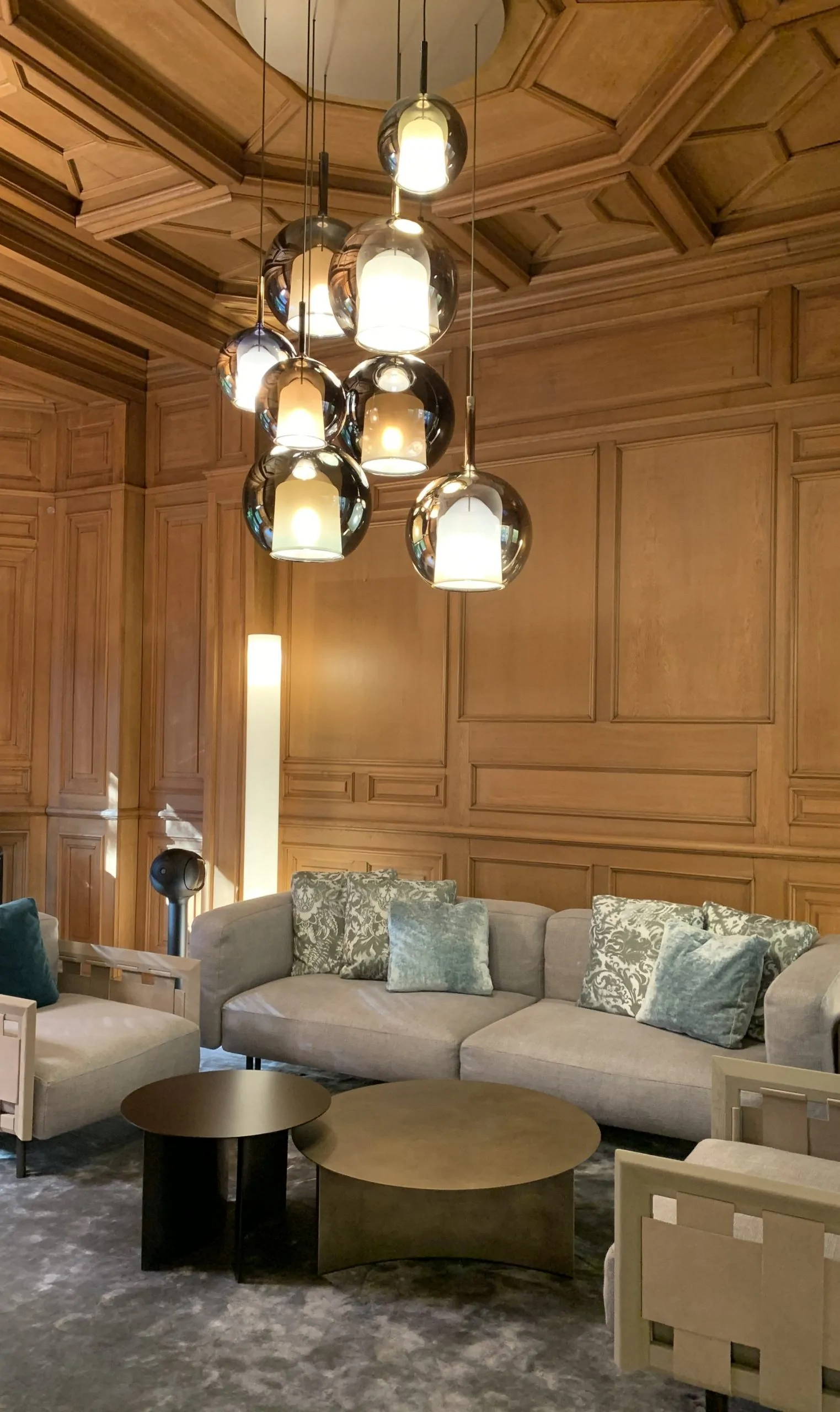 Lounge mit Holzvertäfelung, Ecksofa und Leuchtentraube aus Glaskörpern