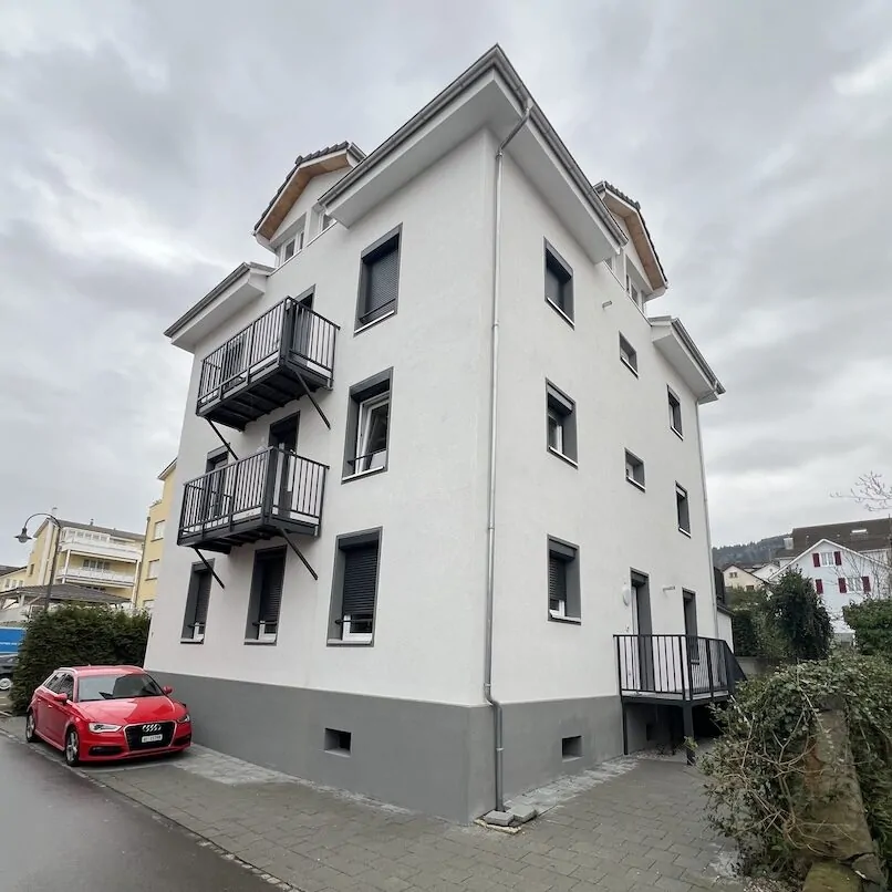 Saniertes Mehrfamilienhaus mit weisser Fassade, Balkonen und grauem Sockel