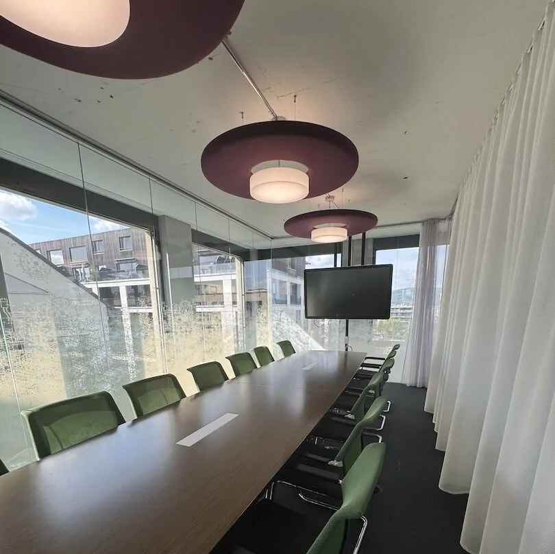 Sitzungszimmer mit langem Tisch, grünen Stühlen und roten Deckenleuchten