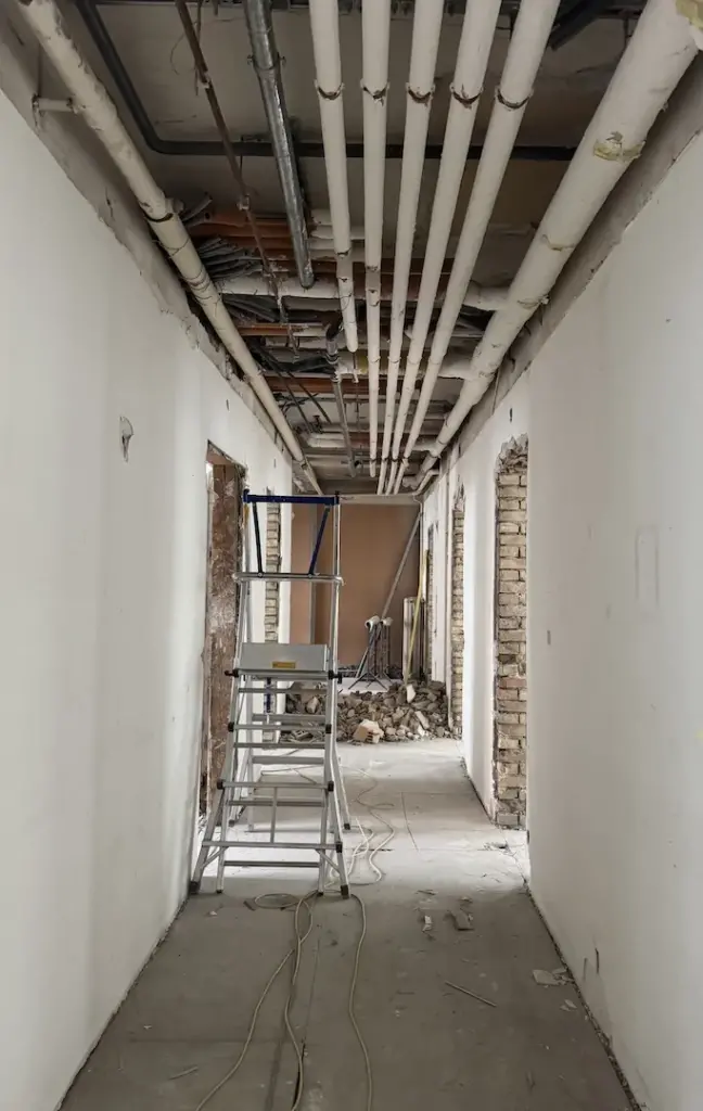Korridor im Rohbau mit offener Decke, Leitungen und Baugerüst