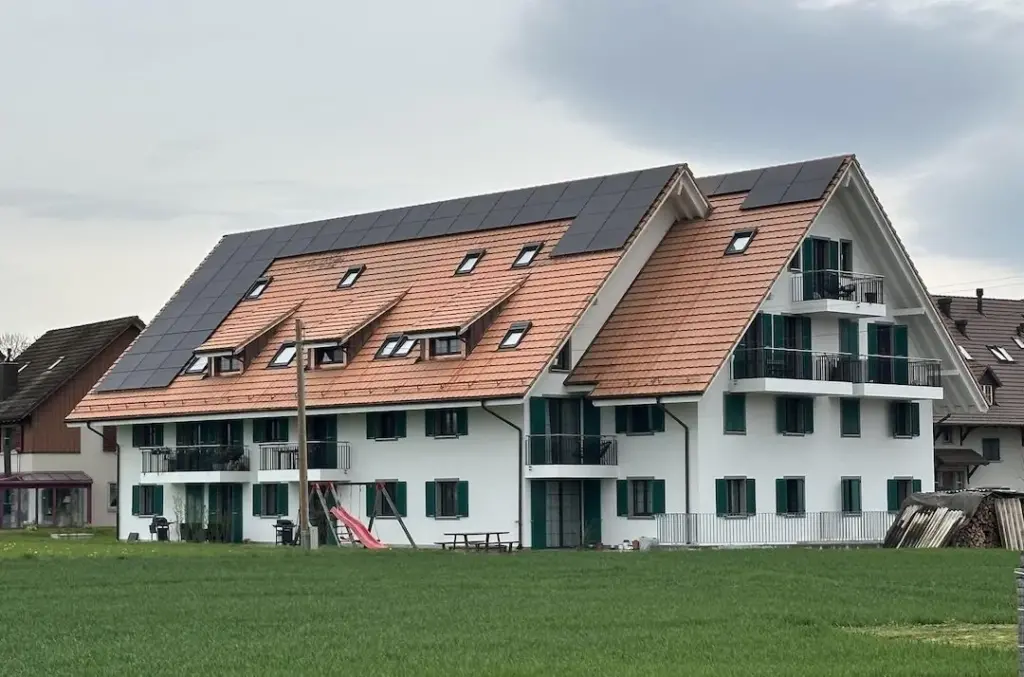 Mehrfamilienhaus mit Ziegeldach und grünen Fensterläden von der Wiese aus