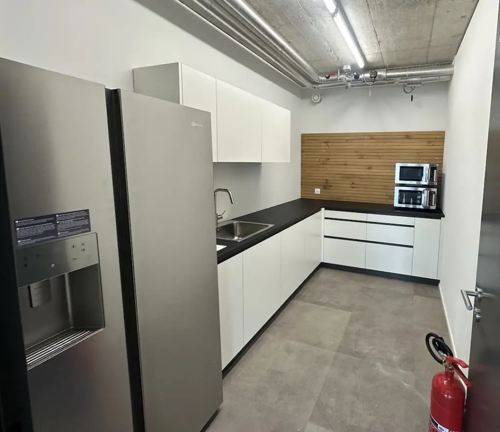 Teeküche nach dem Umbau mit weissen Fronten, Kühlschrank und Holzwand